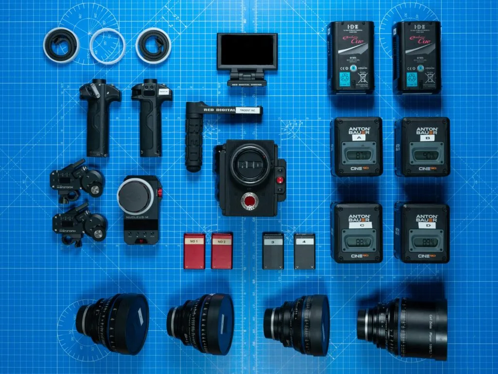 A collection of film cameras, lenses, and equipment arranged on a blueprint surface.