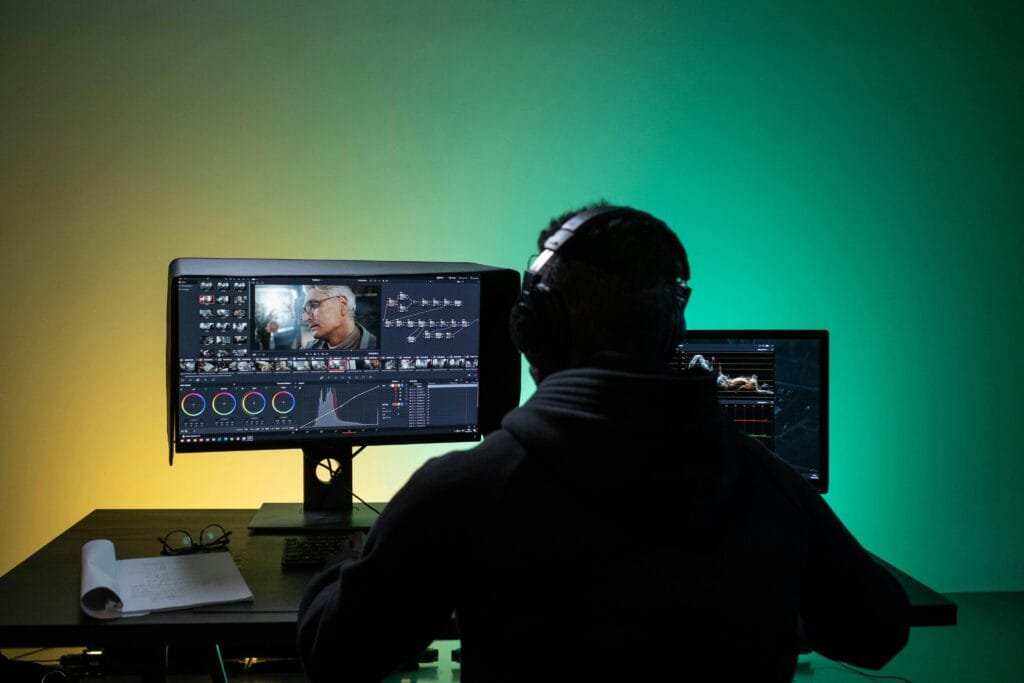 pexels-photo-8102677-8102677 A video editor works on dual monitors with headphones, focusing on color correction.